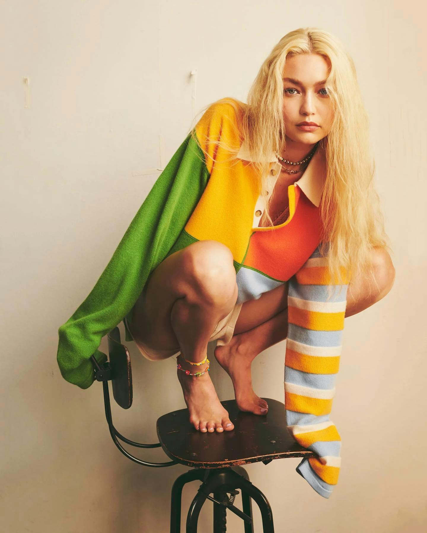 Woman crouching on chair in colorful sweater.