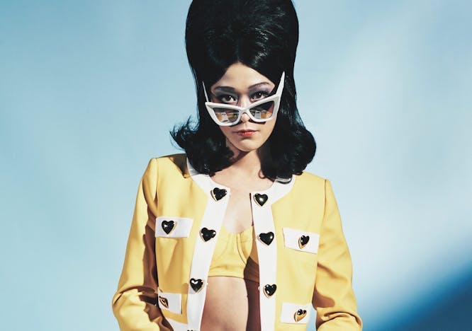 A model in white sunglasses and a yellow cardigan and skirt