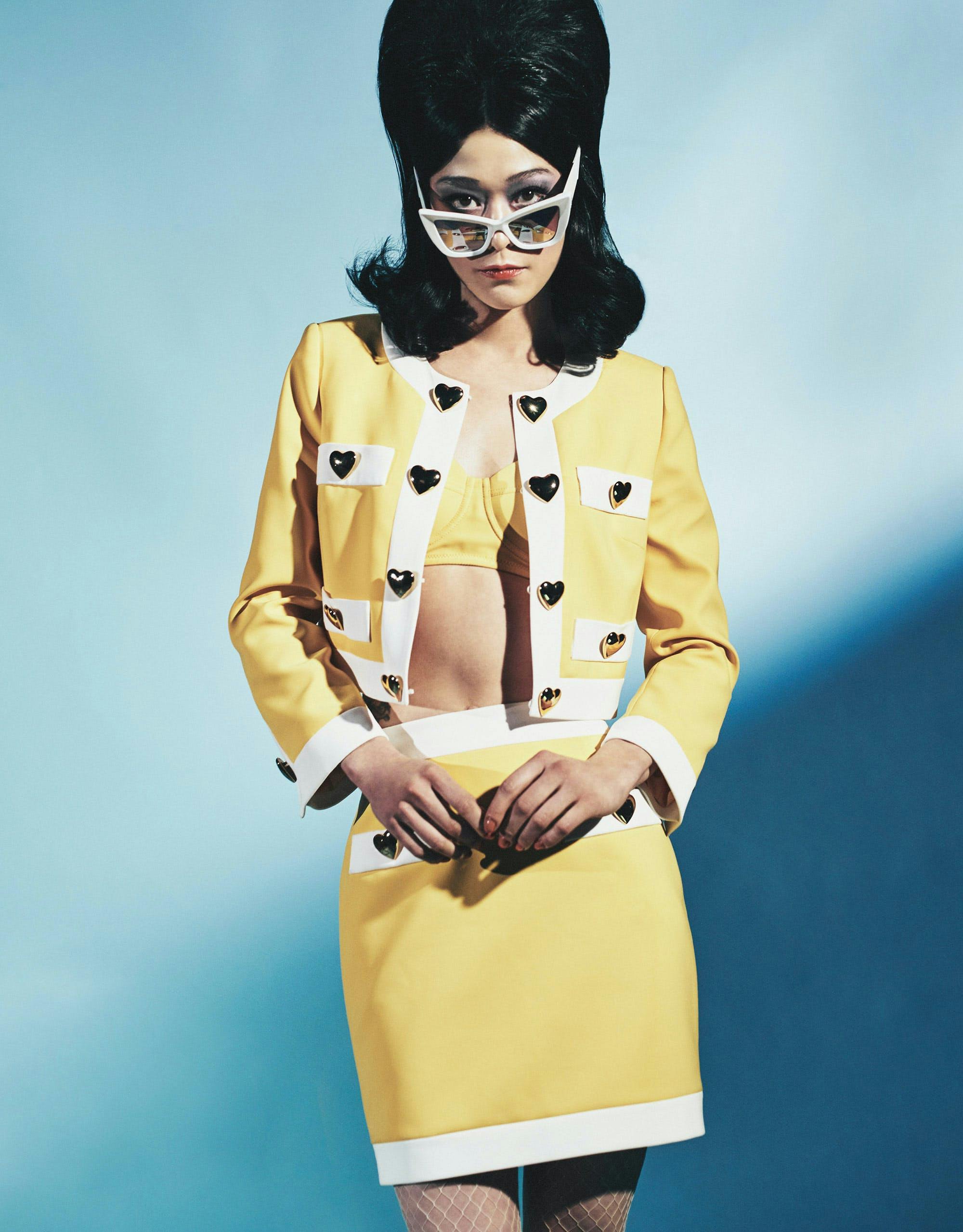 A model in white sunglasses and a yellow cardigan and skirt