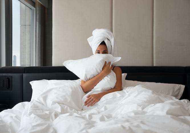 woman in bed white blanket holding a white pillow