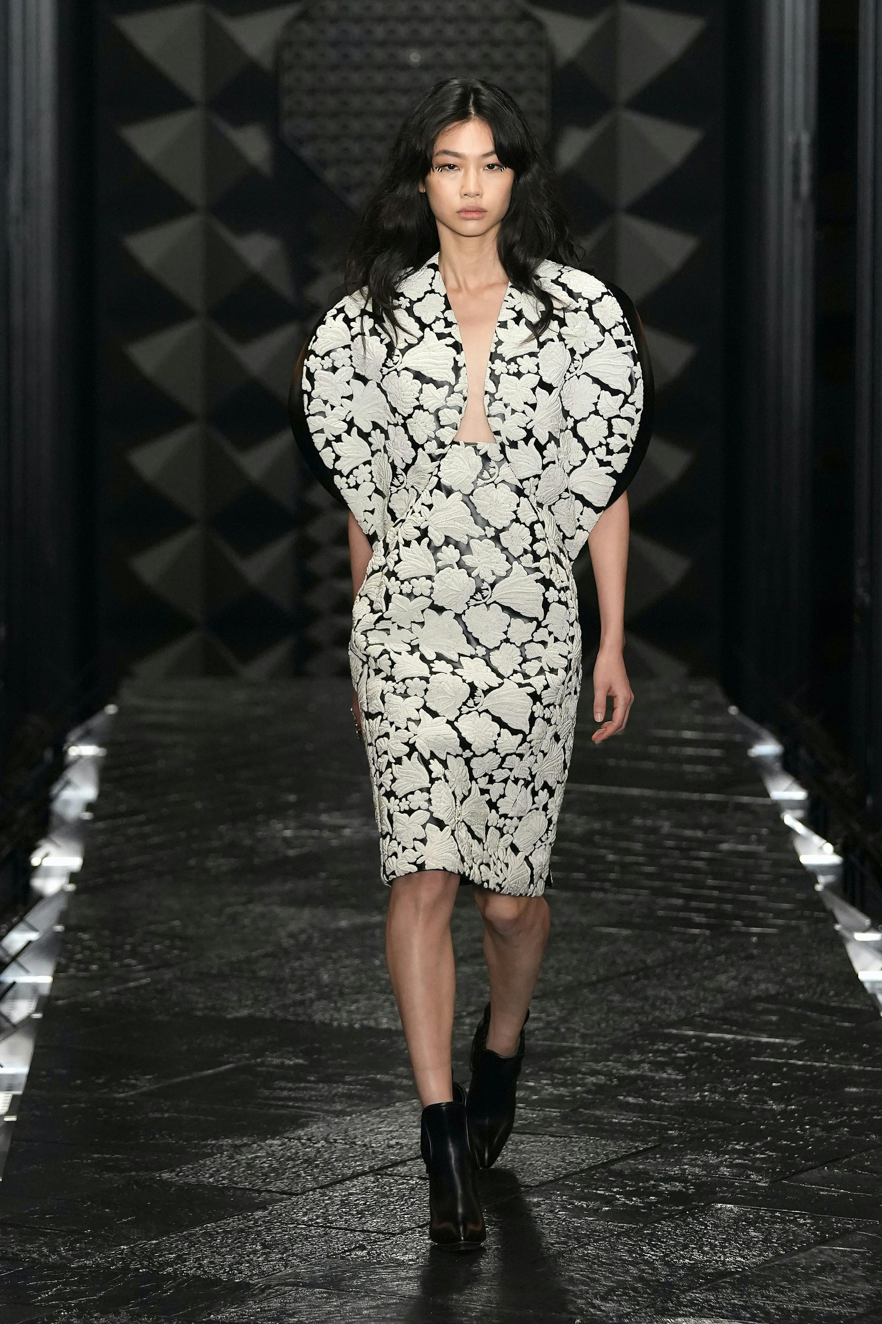 Model wears black and white flowered knee-length dress with black boots.