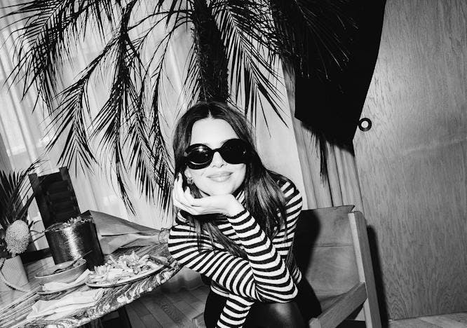 Black and white photo of a woman in a striped shirt sitting down wearing sunglasses.