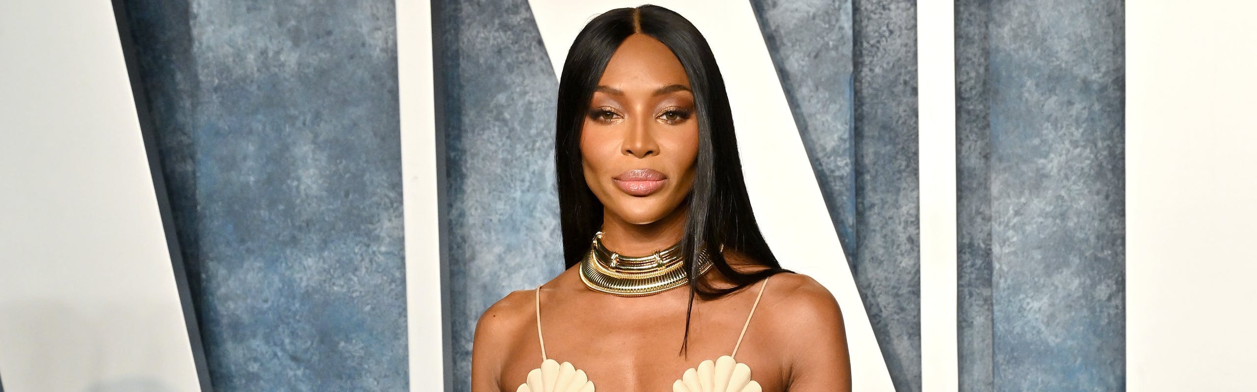 Naomi Campbell wears a white, long dress with tile detailing.