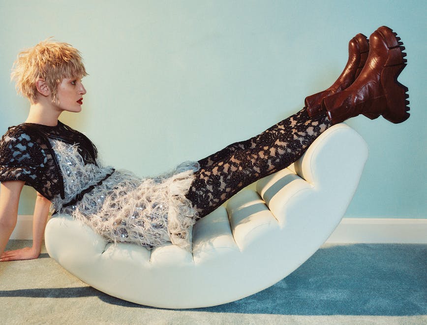 A model sitting in a feather mini dress, lace tights, and chunky boots.