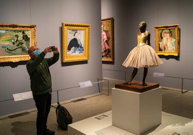 Man taking a picture of Degas' "The Little Dancer" at The Metropolitan Museum in NYC.