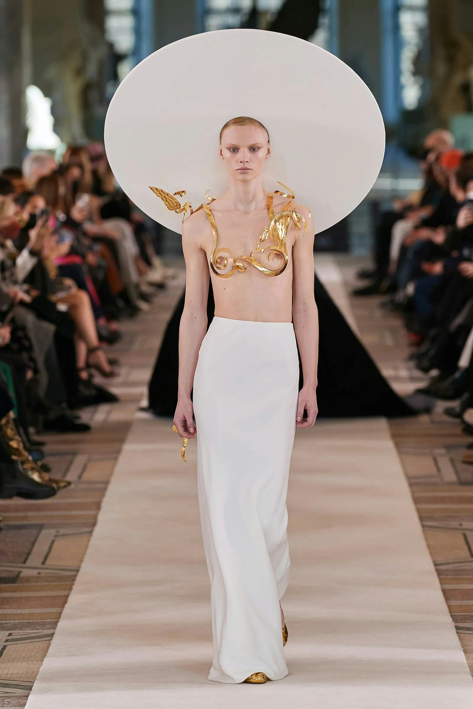 A model in a gold bra top and white skirt for Schiaparelli.