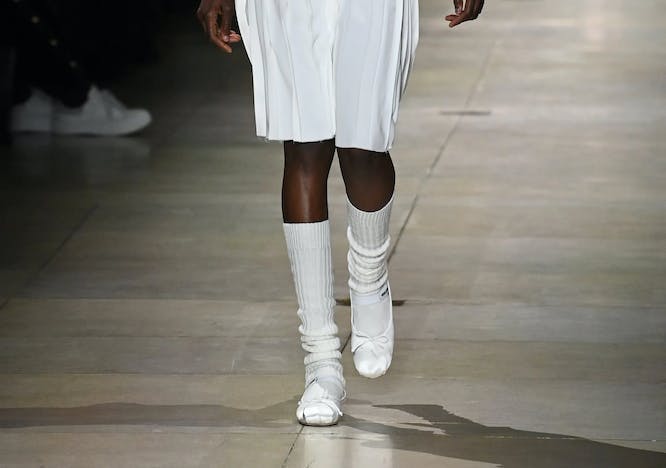 model in white flats, white polo shirt, and white knee length skirt