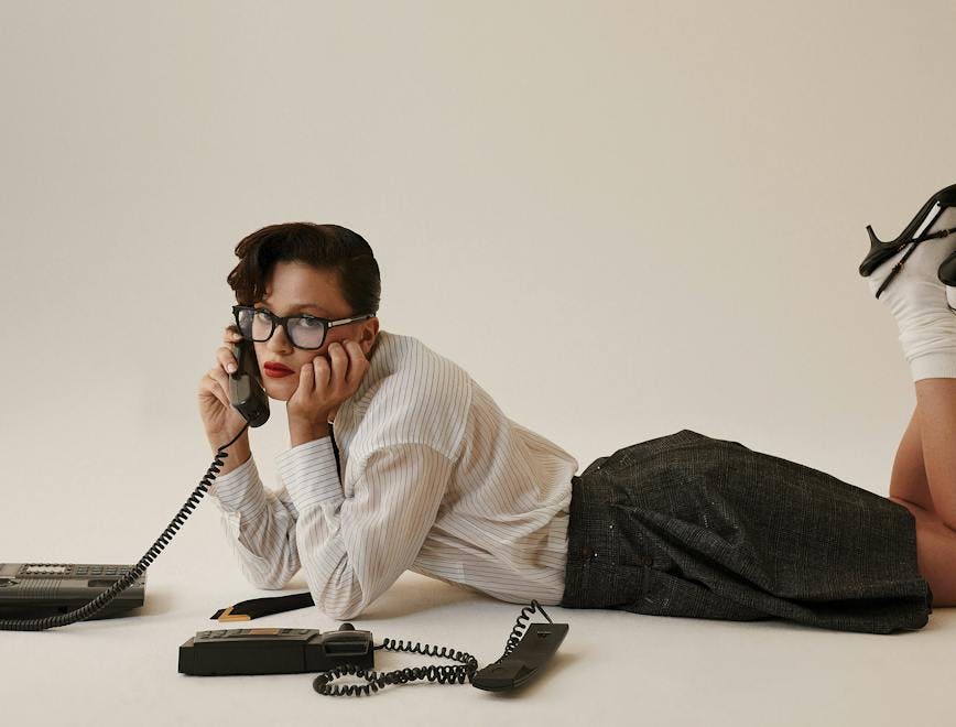 Model holding a landline phone in a shirst, skirt, heels, and glasses