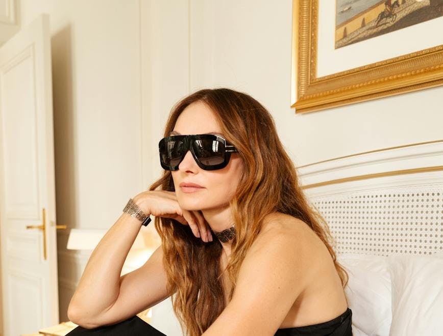 kelly wearstlet in black shades and dress sitting on a bed