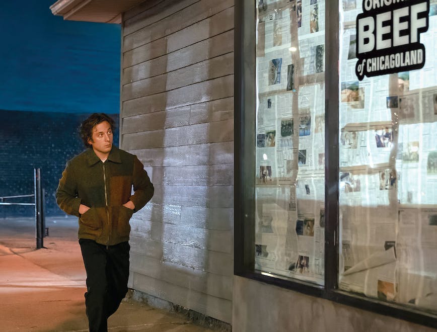Jeremy Allen White as Carmy walking outside of sandwich shop with a sign that reads "The Original Beef of Chicagoland