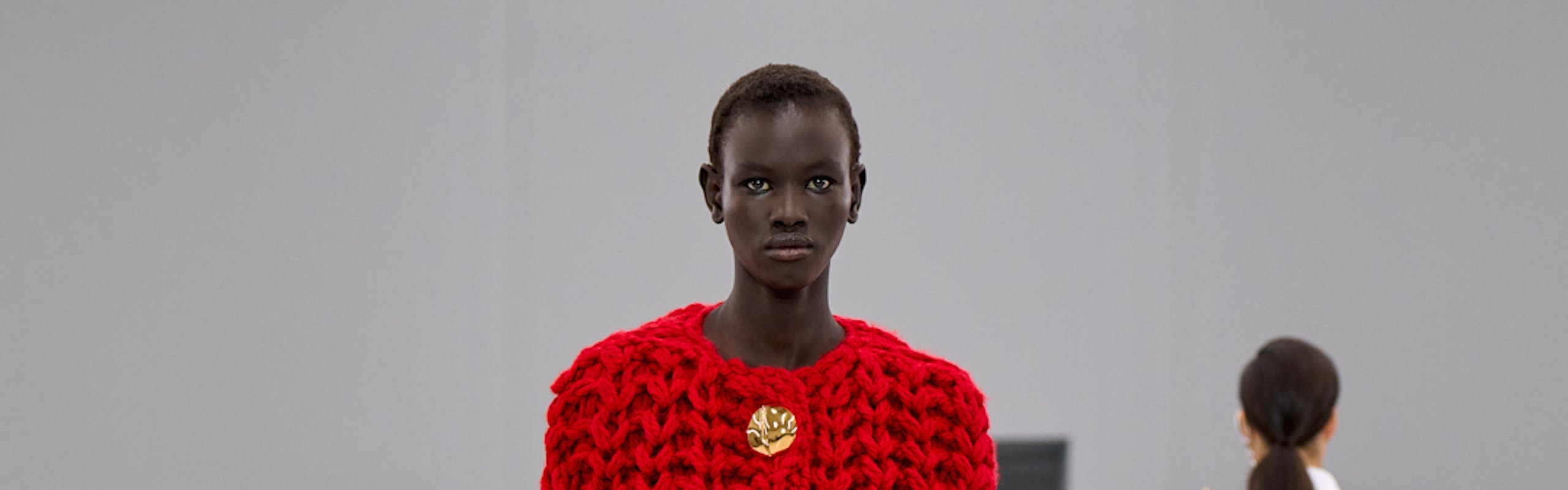 a model in red chunky knit with no sleeves and dark denim