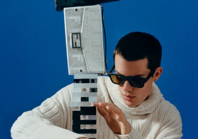 Model with white sweater and sunglasses holding a column with purses stacked on top