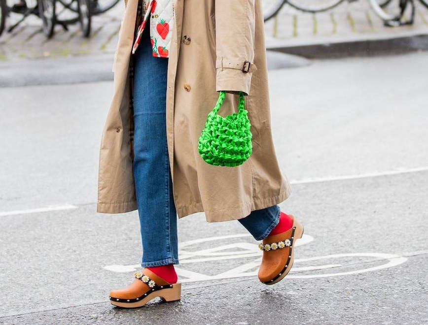 a woman in a trench coat, printed shirt, jeans, and clogs