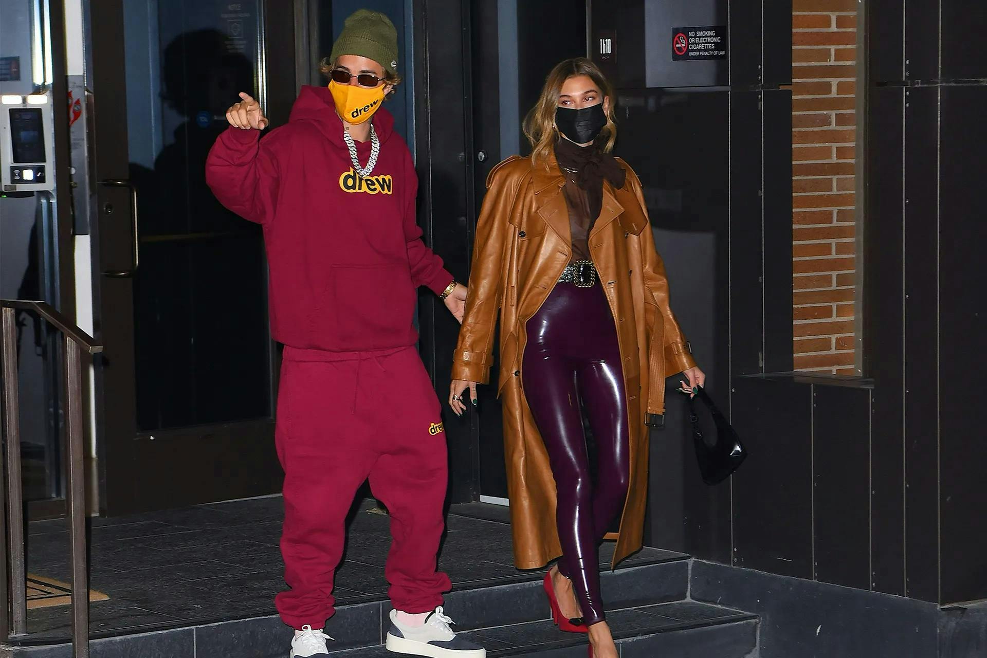 justin bieber in a red sweatshirt and sweatpants and hailey bieber in a brown leather coat and wine red leather pant