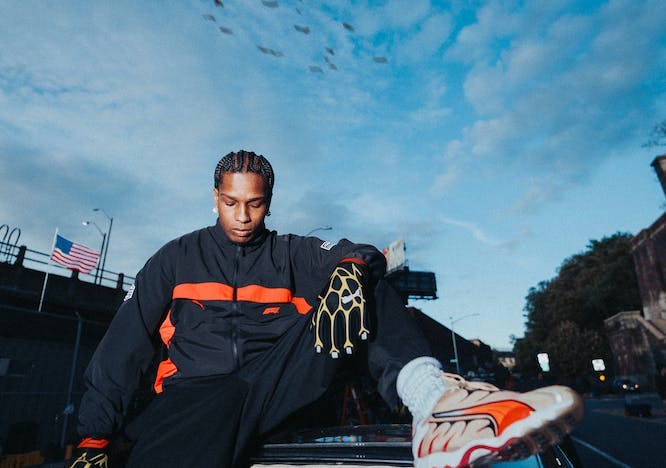 asap rocky in a black and orange racing suit sitting atop a car