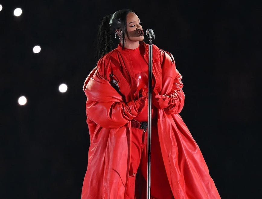 rihanna in a red jumpsuit, overcoat, and bustier