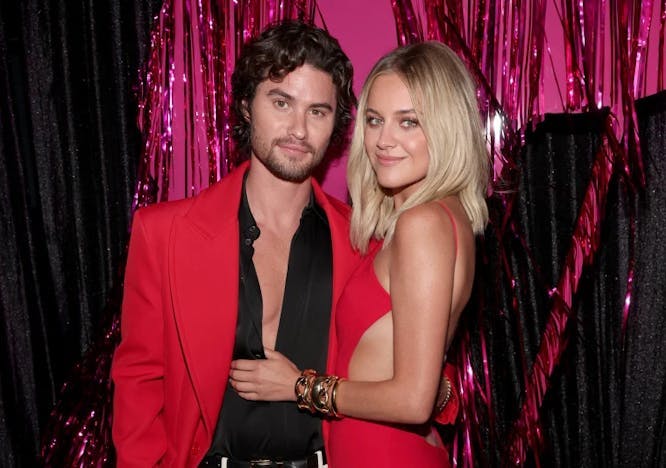 chase stokes in red blazer and black button down next to kelsea ballerini in red dress