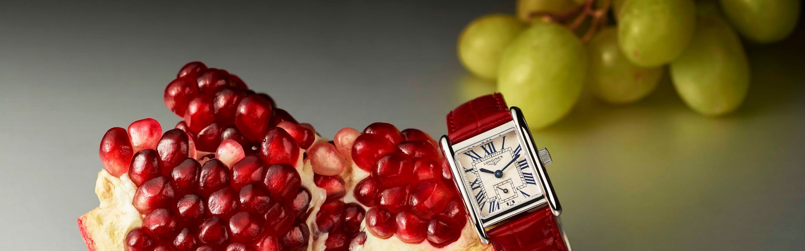 pomegranete and green grapes next to longines watch