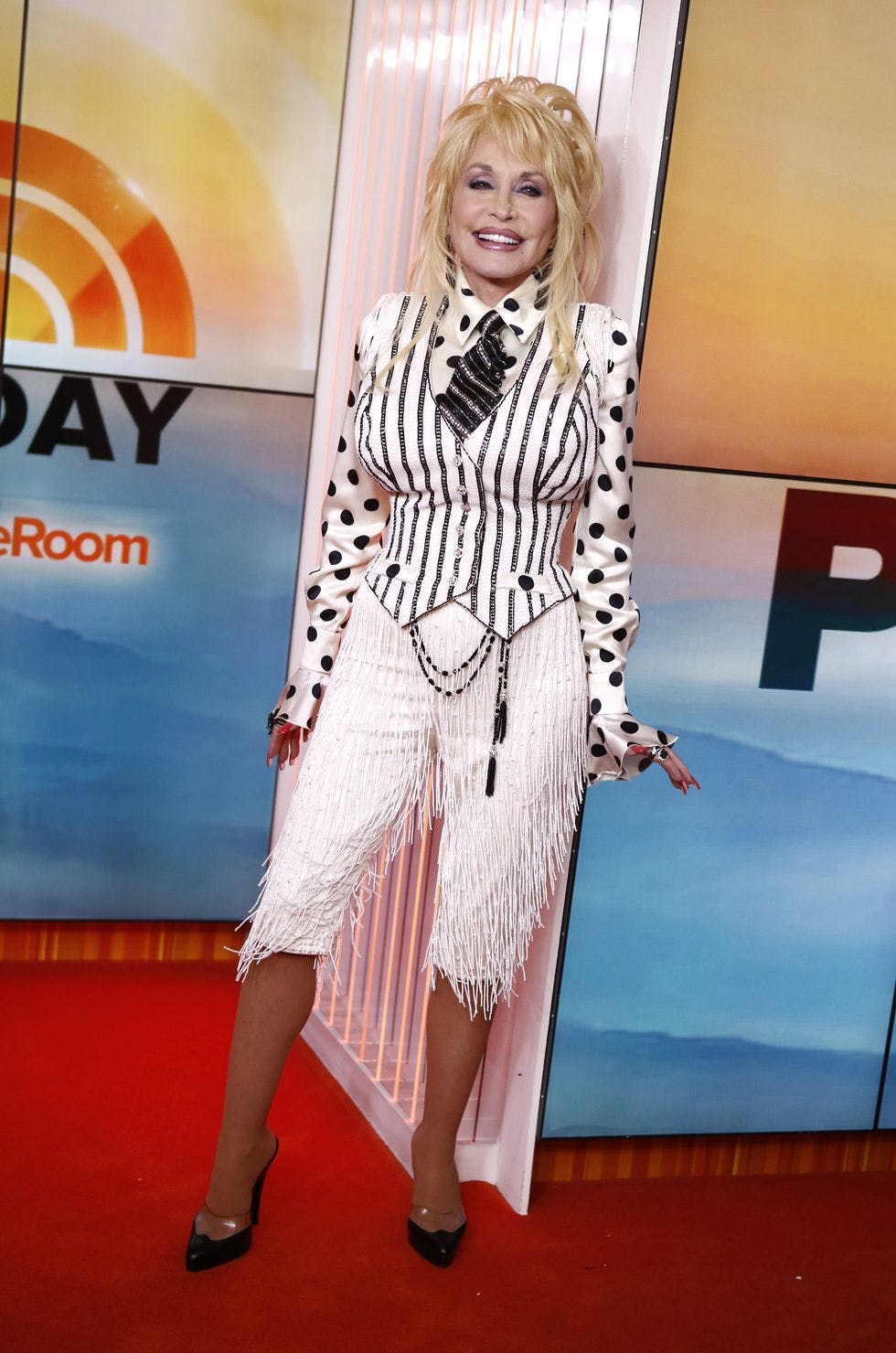 dolly parton in black and white vest, polka dot shirt, and fringe pants