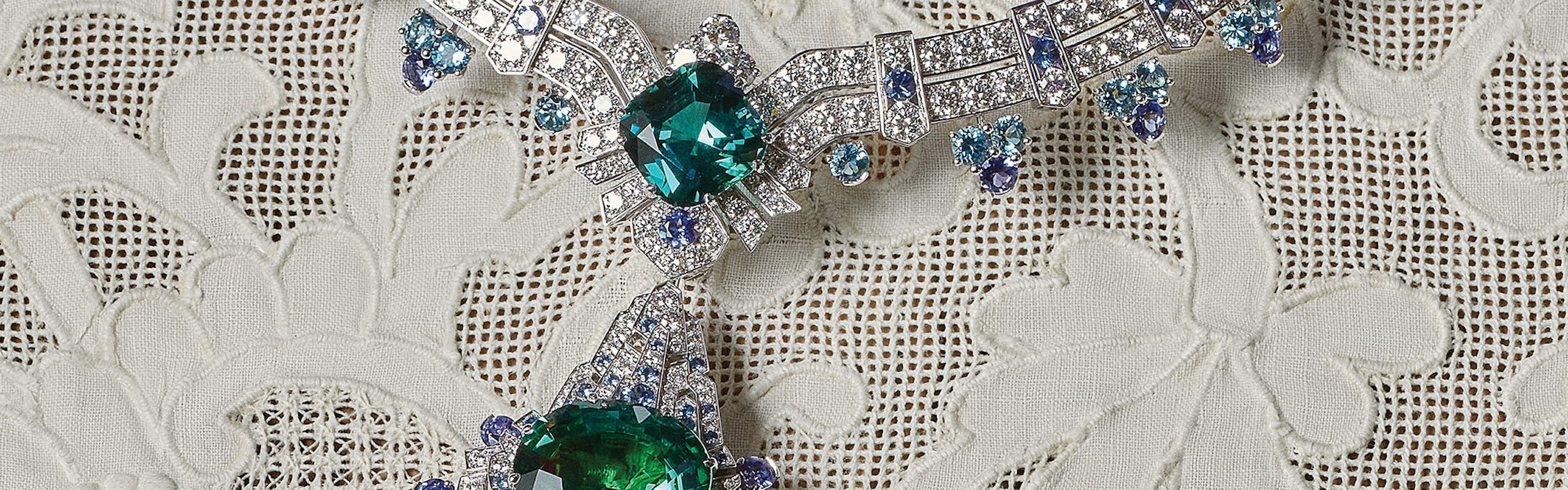 an emerald necklace with diamonds atop a lace cloth on a table
