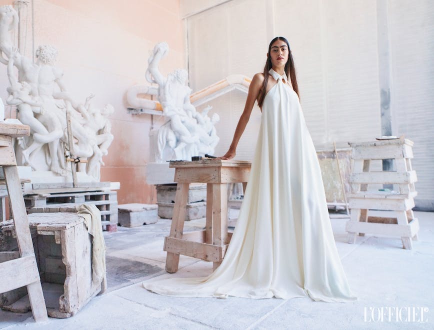 model posing wearing long white dress in sculpture studio