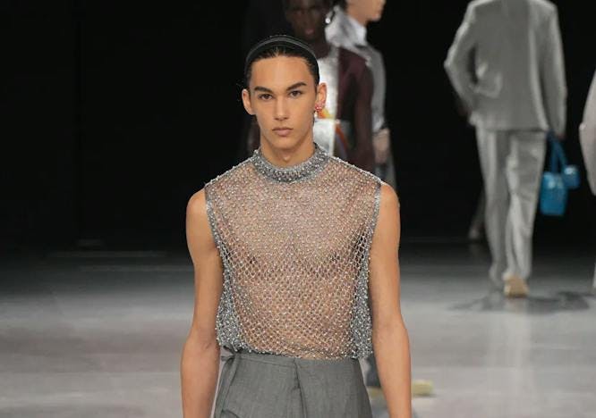 model on runway wearing mesh rhinestone top and gray pants
